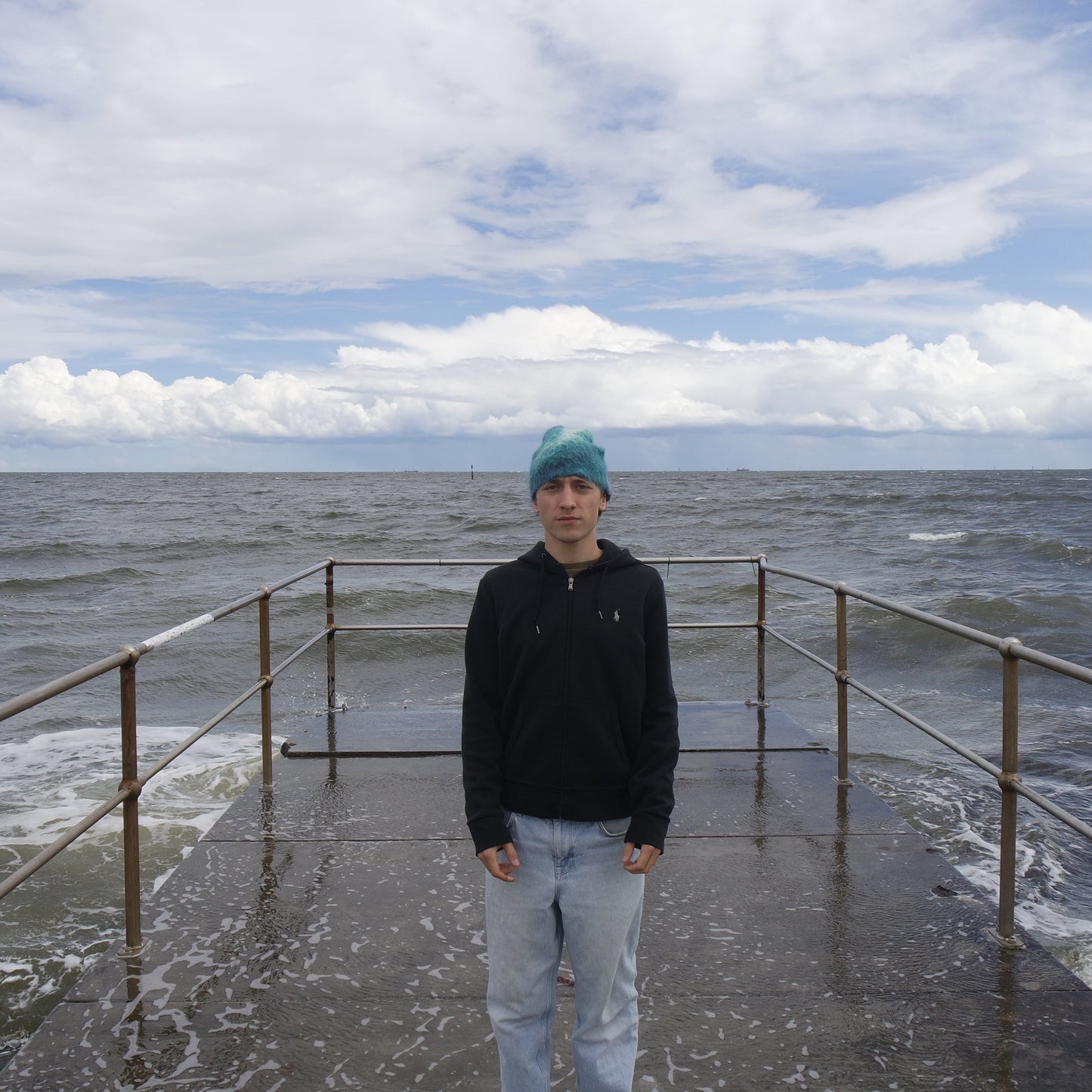 Person standing on a dock by the sea with a cloudy sky